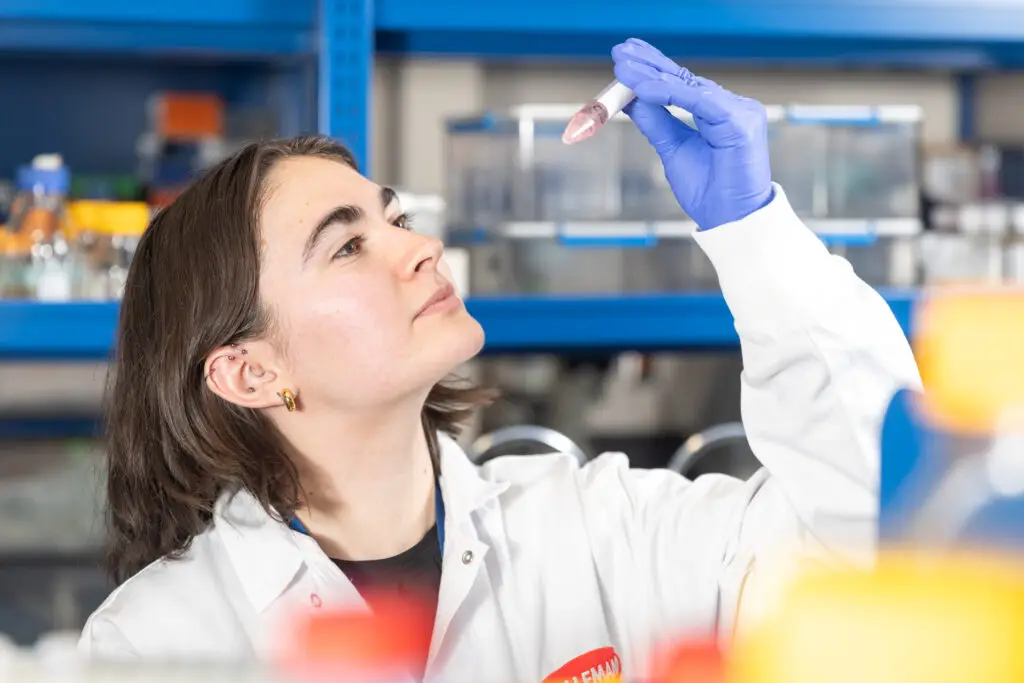 Chercheuse en blouse blanche examinant attentivement un échantillon dans un tube à essai en laboratoire. / Researcher in a lab coat carefully examining a sample in a test tube in a laboratory.